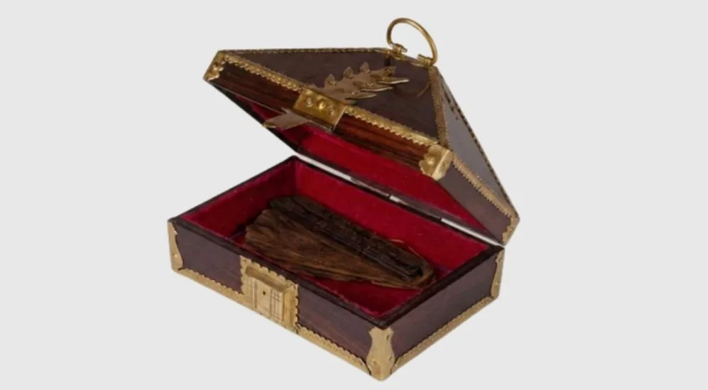 A carved wooden chest lined in red, holding a palm-leaf manuscript
