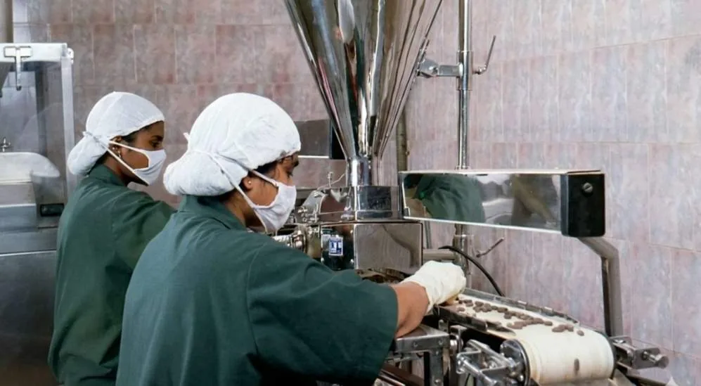 Two members of staff in hairnets and masks operating a packaging machine